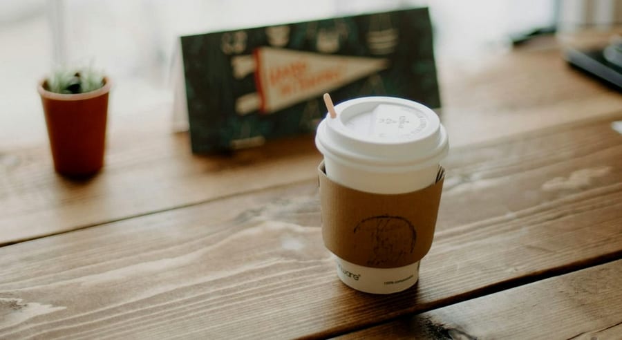 A takeaway coffee and a small cactus on a wood counter